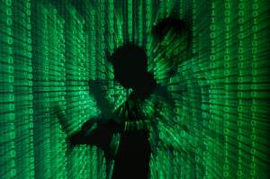 File illustration of a projection of binary code around the shadow of a man holding a laptop computer in an office in Warsaw